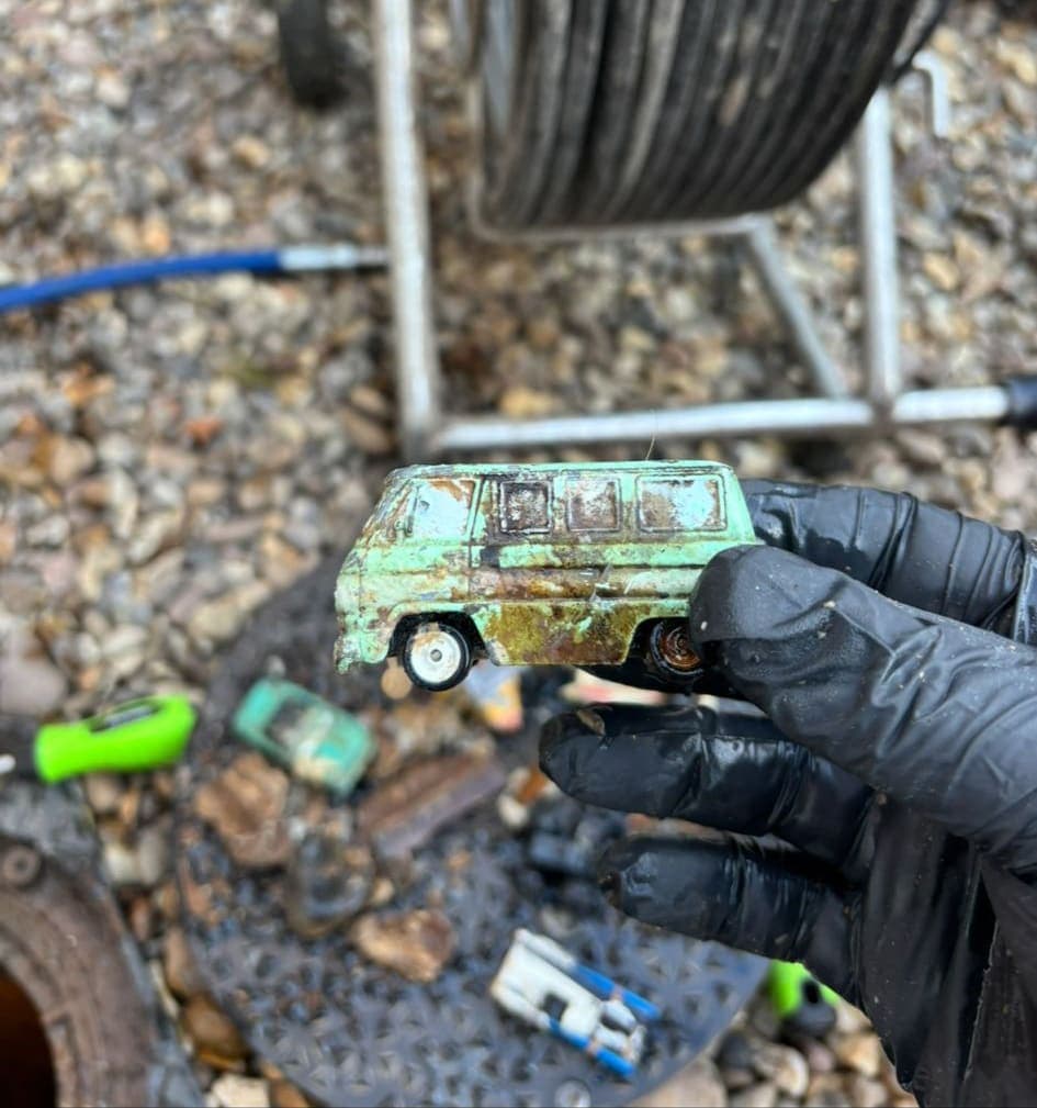 Drainage Engineer unblocking blocked drain holding the toy car that was part of the blocakage.